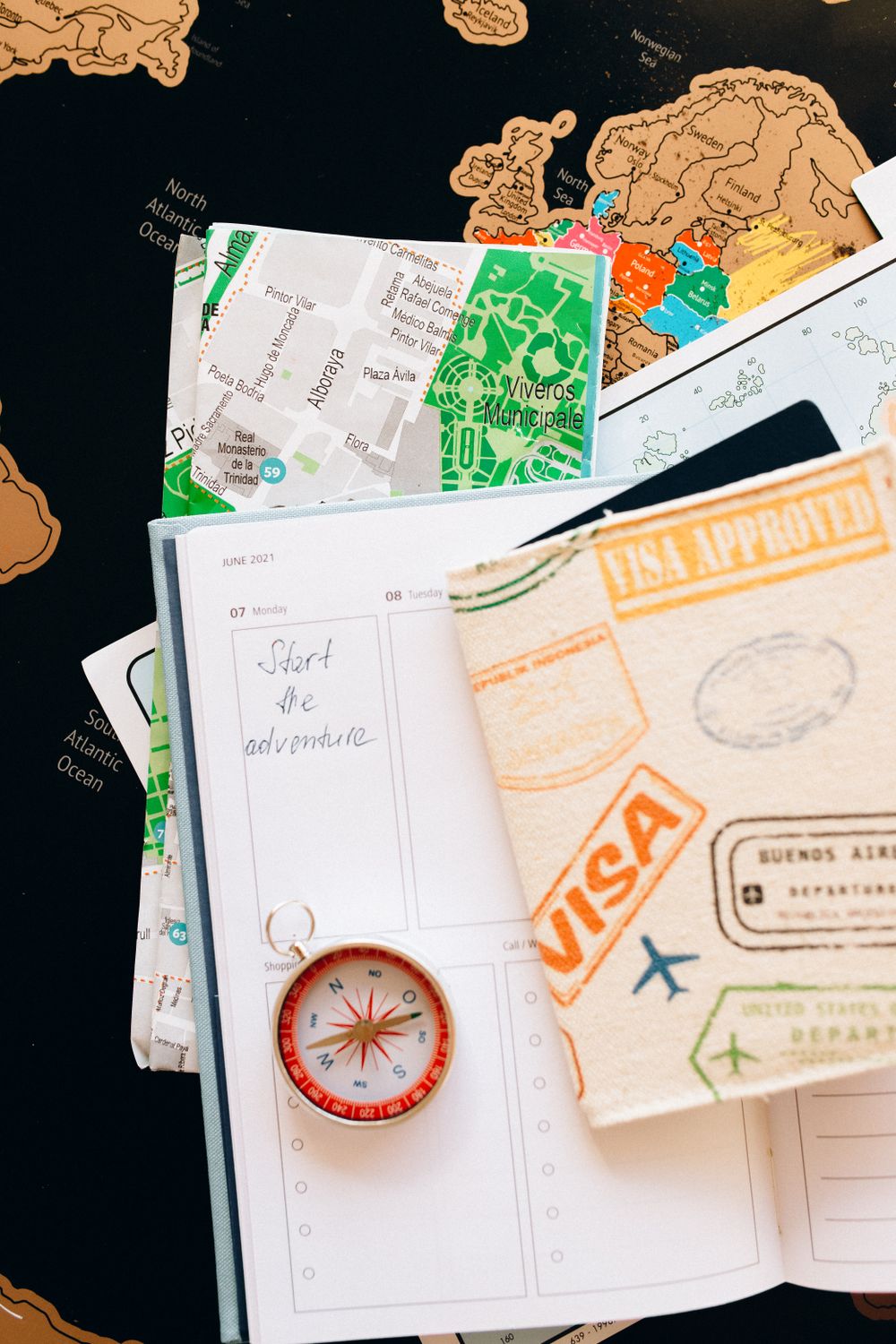 Una agenda abierta con una brújula encima, mapas doblados y un pasaporte con sellos de visa, sobre un mapamundi